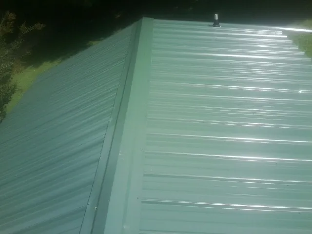 New green metal panels meeting at the ridge of a roof — Flat Roof Repair work by our crew in Nicholson